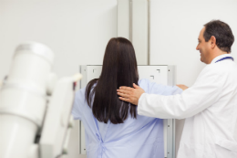 Foto de uma paciente de costas fazendo o exame de mamografia ao lado do médico