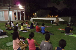 Foto de pessoas sentadas nos jardins da Reitoria fazendo meditação