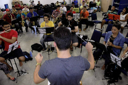 Imagem: Professor regendo alunos enquanto eles tocam instrumentos musicais em uma sala de aula (Imagem: Banda Sinfônica da UFC)