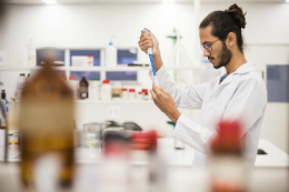 Imagem: foto de um homem de barba vestindo jaleco branco e manipulando itens em um laboratório