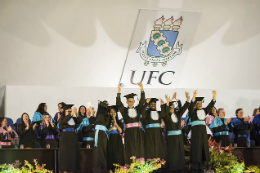 Imagem: Foto de estudantes vestindo becas no palco da Concha Acústica em solenidade de Colação de Grau