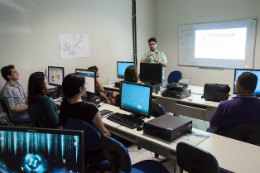 Imagem: servidores em laboratório de informática e professor à frente dos computadores dando aula
