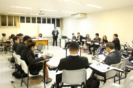 Imagem: Foto de evento da SONU - uma sala de aula com estudantes sentados em circulo vestindo roupas alinhadas e uma pessoa em pé