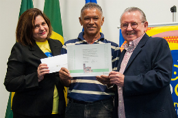 Imagem: Foto de servidor recebendo certificado entre o reitor Henry Campos e a pró-reitoria de gestão de pessoas Marilene Feitosa