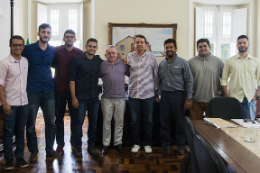 Imagem: nove homens em pé posam para foto no gabinete do reitor 