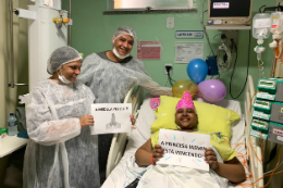 Imagem: foto de uma leito de hospital com paciente e equipe médica. Ao fundo, balões decoram o quarto.