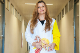 Imagem[: Professora Tatiana Zylberberg em um corredor, segurando uma peça anatômica que reproduz um útero (Foto: Viktor Braga/UFC)