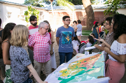 Foto do reitor Henry Campos e de estudantes vendo um mapa em um estande 