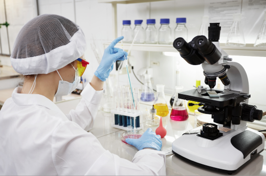 Pesquisadora está de costas em um laboratório para utilizar um laboratório e analisar o conteúdo de tubos de ensaio com líquidos coloridos