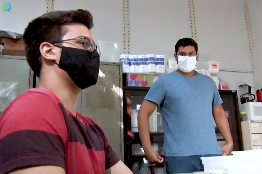 Imagem: Dois estudantes de máscara sendo entrevistados dentro do laboratório