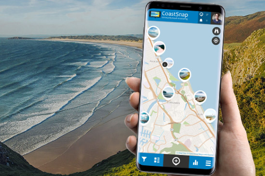 Foto de uma pessoa segurando o celular na palma da mão e ao fundo uma paisagem de praia