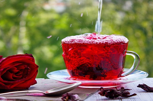 Imagem: Xícara contendo chá de hibisco; ao lado há uma colher e uma flor de hibisco (Foto: Natalia Osipova/Pixabay)