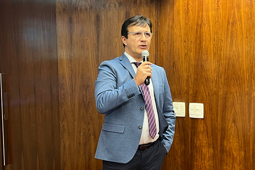 Imagem: Foto do reitor Custódio, de terno azul e gravata listrada, em pé segurando um microfone