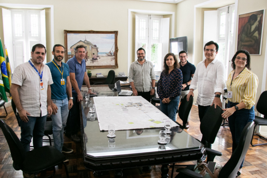 Imagem: Foto da reunião do reitor Custódio Almeida com o secretário municipal de Infraestrutura, Samuel Dias, com um grupo em pé perante uma mesa de reuniões