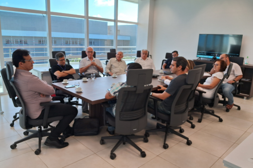 Imagem: Foto da mesa de reunião da FIOCRUZ com os gestores e técnicos sentados em uma grande mesa retangular de madeira e com cadeiras de escritório pretas