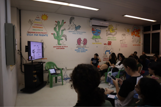 Imagem: Sala de vídeo do LABOMAR com os alunos sentados em carteiras assistindo à televisão 