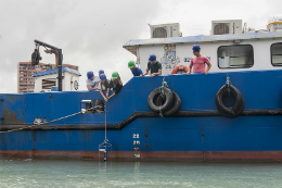 Imagem: foto de um barco azul e pesquisadores içando um recipiente com água do mar
