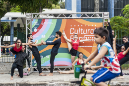 Imagem: foto de dançarinos em frente a um banner do Corredor Cultural