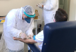 Imagem de profissional da saúde aplicando teste na veia do braço de uma pessoa sentada