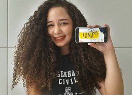 Imagem: foto de uma jovem de cabelos longos e cacheados segurando um celular 