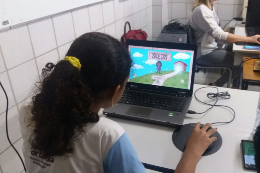 Imagem: uma criança com farda escolar a aprece de costas, olhando para a tela de um computador