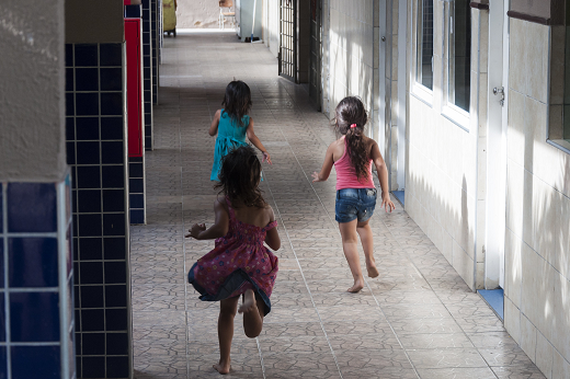 Imagem: três crianças correndo por um corredor do IPREDE; na imagem, as crianças aparecem de costas (Foto: Viktor Braga/UFC)