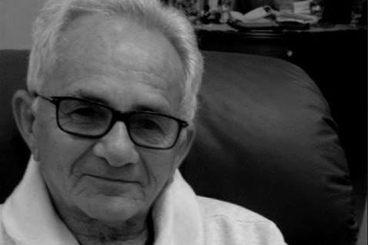 Imagem: Homem velho com blusa branca e óculos de armação preta, cabelo branco
