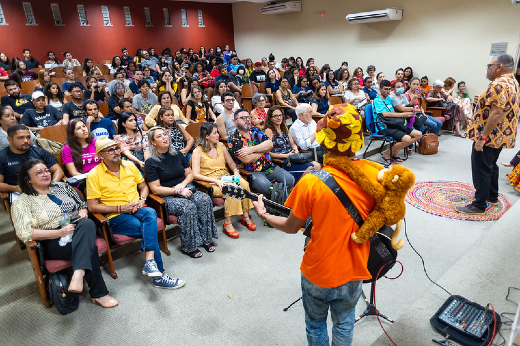 Imagem: plateia em auditória assiste à apresentação de um violeiro