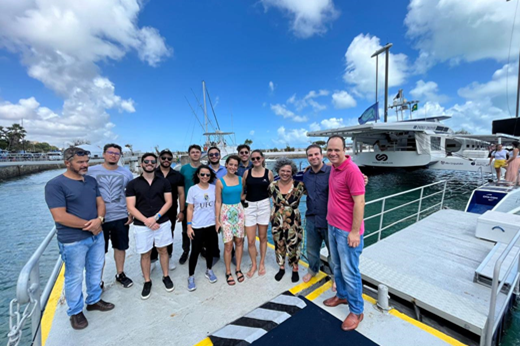 Imagem: Grupo de 13 pessoas, dentre elas a vice-reitora Diana Azevedo, posa no ancoradouro durante visita ao navio Energy Observer. (Foto: Divulgação)