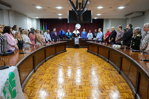 Imagem: Participantes da solenidade, dispostos em semicírculo, cantam o hino nacional de pé