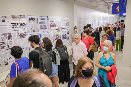 Imagem: Pessoas visitam a exposição Sementes de Lutas; algumas delas leem informações em um painel que mostra uma linha do tempo do movimento estudantil na UFC.