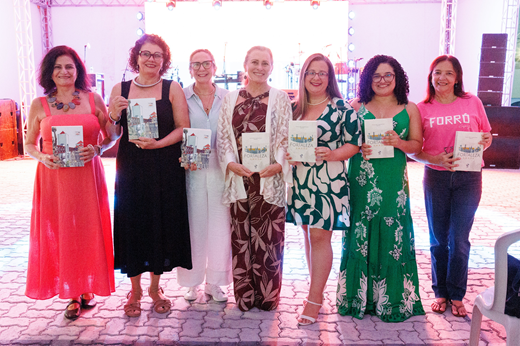 Imagem: Sete das autoras do livro posam com seus exemplares em frente ao palco