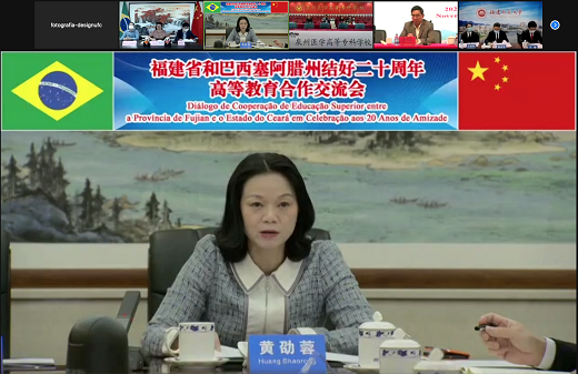 Foto mostra uma das representantes chinesas que conduziu o evento, com banner em mandarim e português, na parte superior, em que é informado o nome do evento