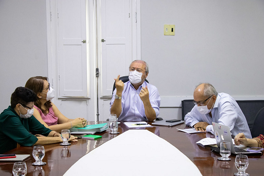 Imagem mostra quatro pessoas sentadas próximo à cabeceira de uma mesa, sendo duas mulheres na esquerda, o reitor Cândido Albuquerque gesticulando ao centro e o vice-reitor Glauco Lobo do lado direito