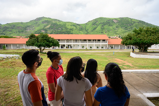 Imagem mostra estudantes de costas olhando para área aberta do campus com uma serra ao fundo
