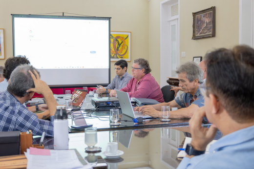 Empresários e reitor sentados à mesa da Reitoria olhando para a apresentação do projeto