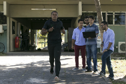 Imagem: foto de grupo de três estudantes com um deles segurando um notebook e um homem ao lado correndo