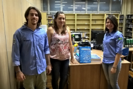 Imagem: Dois estudantes e uma servidora durante entrega de livros à biblioteca