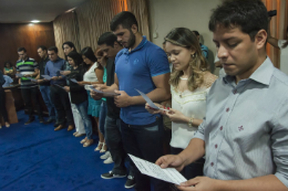 Imagem: Novos servidores lendo a documentação, em pé, durante a cerimônica de posse (Foto: Viktor Braga)