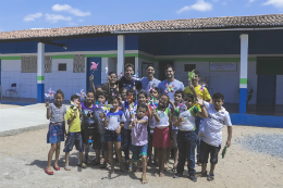 Imagem: Foto de integrantes da equipe e crianças em frente a uma escola de Forquilha