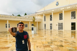 Imagem: Servidor Gleiton Souze segura caneca da UFC em frente ao prédio do curso de Medicina de Sobral