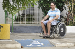 Imagem: Foto do mestre Igor Peixoto sentando na cadeira de rodas próximo a uma rampa com desenho de cadeirante