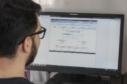 Imagem: foto de um rapaz de costas, olhando tela de computador com sistema SIGAA aberto