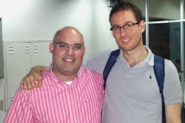 Imagem: dois homens posam para foto. O do lado esquerdo, é baixo careca, gordo e veste camisa rosa. Do lado direito, professor magro, alto, branco. Os dois usam óculos.