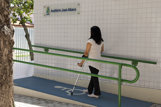 Imagem: Mulher segurando uma muleta, subindo uma rampa de acesso do Auditório José Albano, no Centro de Humanidades (Foto: Jr. Panela/UFC)