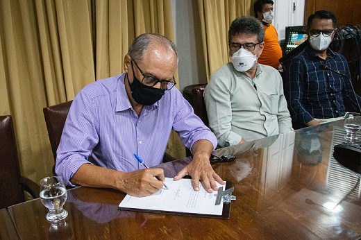 Imagem: homem de camisa lilás assina documento