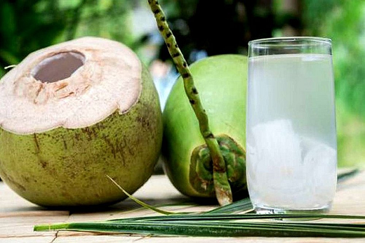Imagem: Copo contendo água de coco; ao lado há dois cocos, sendo um fechado e outro aberto (Foto: Shutterstock)