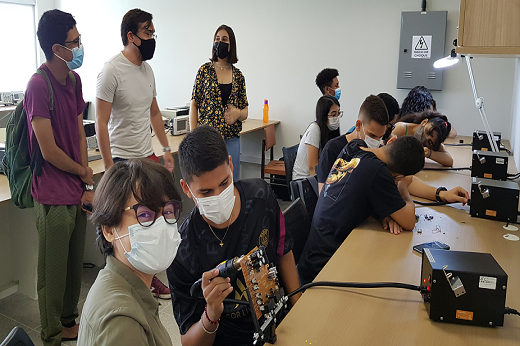 Imagem: Alunos do Curso de Engenharia de Computação realizando atividades em um dos laboratórios do campus; eles estão sentados e outros em pé, mexendo em aparelhos que estão sobre uma bancada de madeira (Foto: divulgação/Campus de Quixadá)