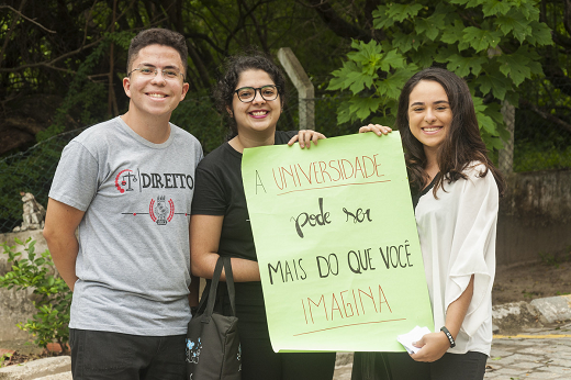 Imagem: Três estudantes, sendo que duas delas seguram um cartaz no qual está escrito 