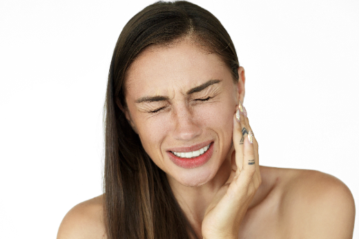 Imagem: Mulher de pele clara e cabelo preto liso colocando a mão no rosto, com expressão de dor (Foto: Freepik)